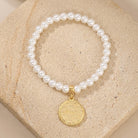 Pearl bracelet with a gold tone peace charm on a beige stone surface