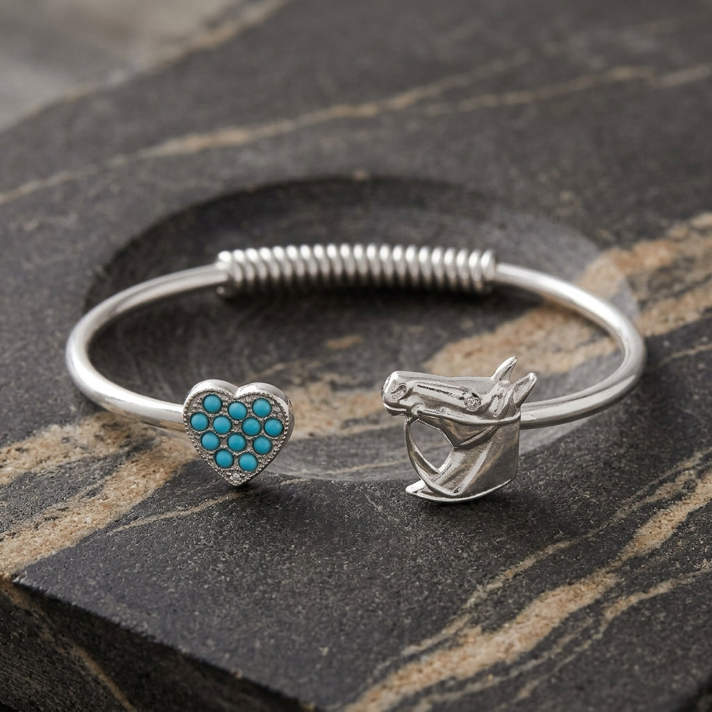 Silver bracelet with heart-shaped and horse head cuff design with turquoise accents on a stone surface