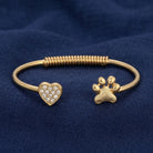 Gold tone heart and pet paw crystal spring bracelet resting on dark navy blue linen surface