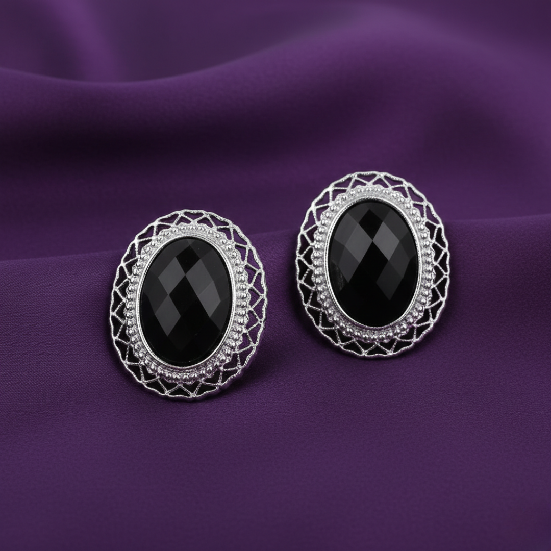 Pair of black gemstone earrings with silver intricate designs on a purple fabric background