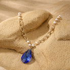 Gold tone link chain with faux pearls and a blue crystal pendant necklace resting on light stone surface