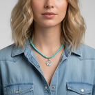 Woman wearing a turquoise beaded necklace with a silver horse head pendant against a neutral background