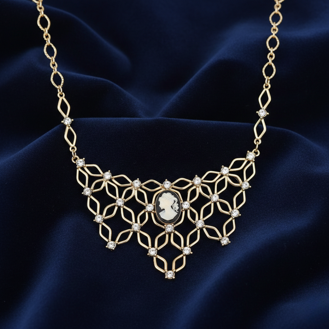 Gold necklace with a central cameo pendant and scattered clear crystals on a dark blue fabric background