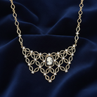 Gold necklace with a central cameo pendant and scattered clear crystals on a dark blue fabric background