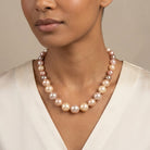 Woman wearing a graduated pink pearl necklace with a white outfit. 