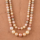 Double strand pink and peach multicolor pearl necklace on a red stone surface