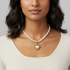 Woman wearing a faux pearl necklace with a heart-shaped pendant on a plain background