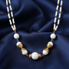 Necklace with white beads and gold accents on a blue fabric background