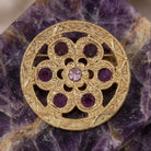 Gold brooch with amethyst crystals on a purple stone background