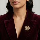 Close-up of a person wearing a burgundy velvet blazer with a gold brooch that has amethyst crystals.
