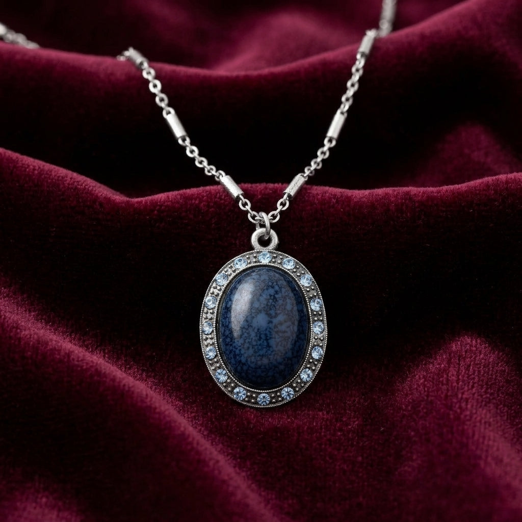 Necklace with a blue stone pendant with crystal accents on a burgundy fabric background