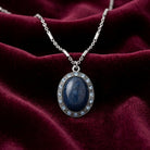 Necklace with a blue stone pendant with crystal accents on a burgundy fabric background