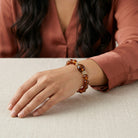 Person wearing a brown beaded bracelet on a neutral background