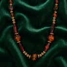 Brown and gold tone beaded necklace resting on dark green satin fabric