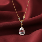 Gold necklace with a teardrop-shaped crystal pendant on a red fabric background