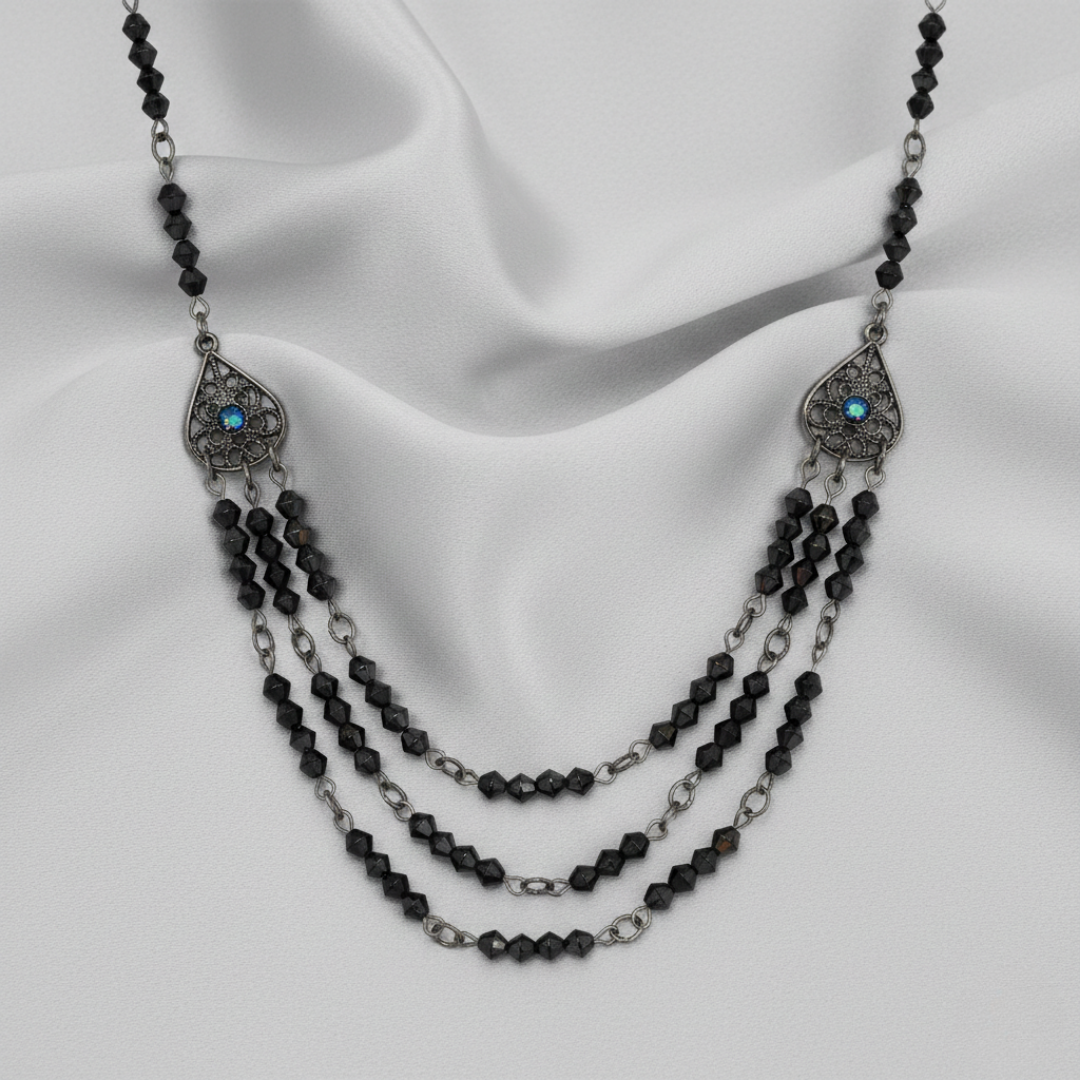 Bib necklace with black beads and silver chain on a white fabric background