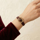 Hand wearing a brown bracelet with an oval brown obsidian gemstone and a gold tone frame on a beige background