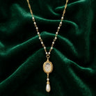 Gold necklace with faux pearls and a dangling faux pearl pendant on a green velvet background