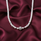 Faux pearl necklace with a silver clasp on a burgundy satin background