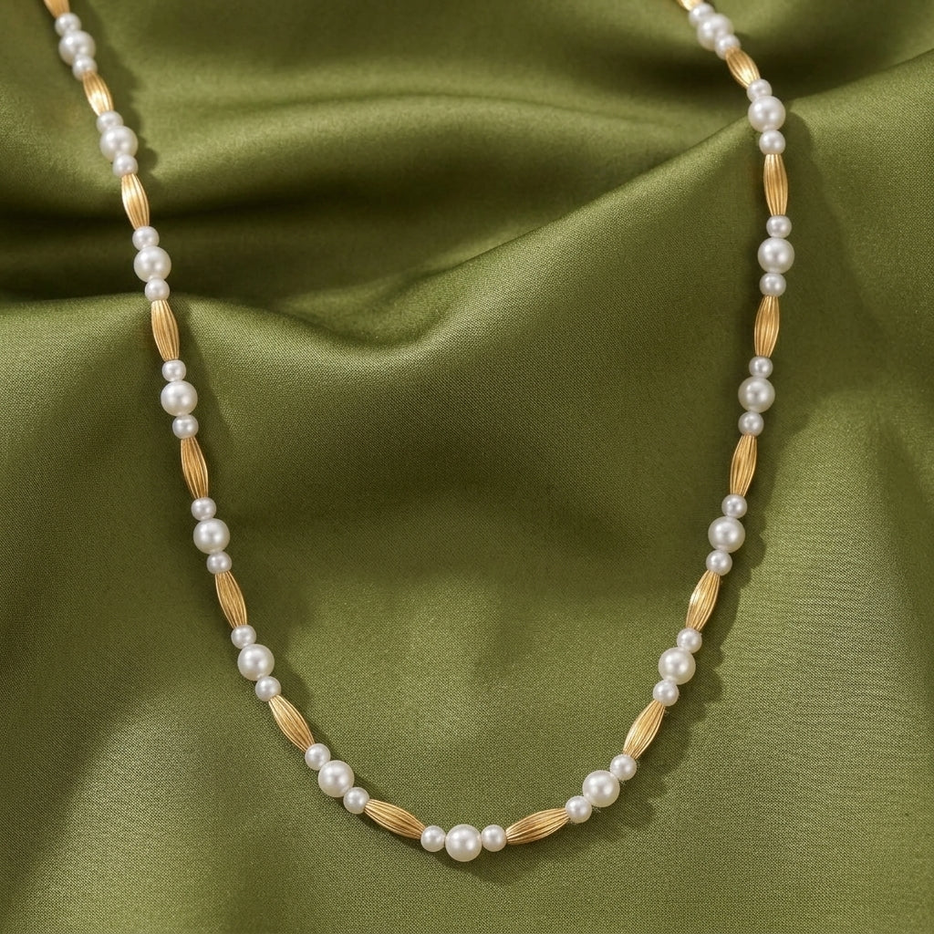 Pearl necklace with gold tone beads against an olive green fabric 