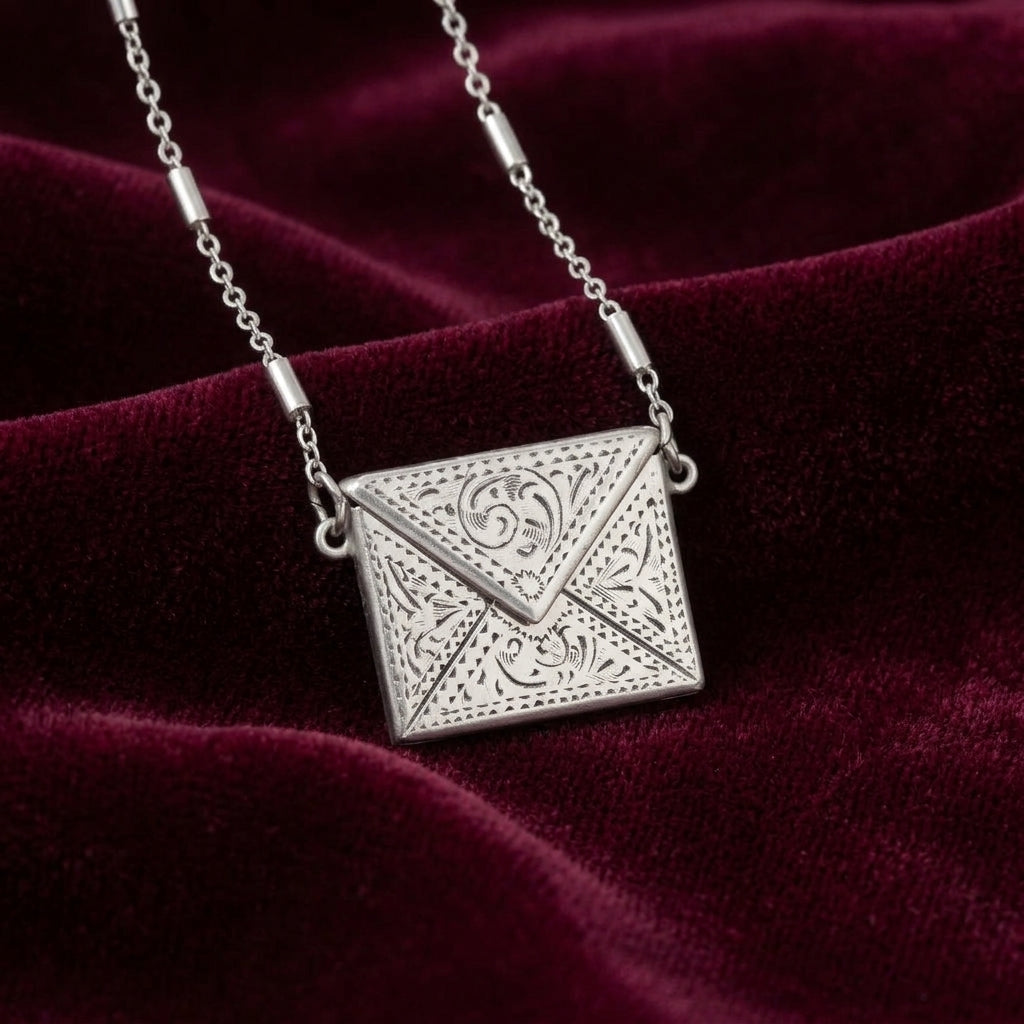 Silver envelope-shaped pendant on a chain against a burgundy fabric background