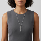 Person wearing a silver necklace with a key pendant on a plain background