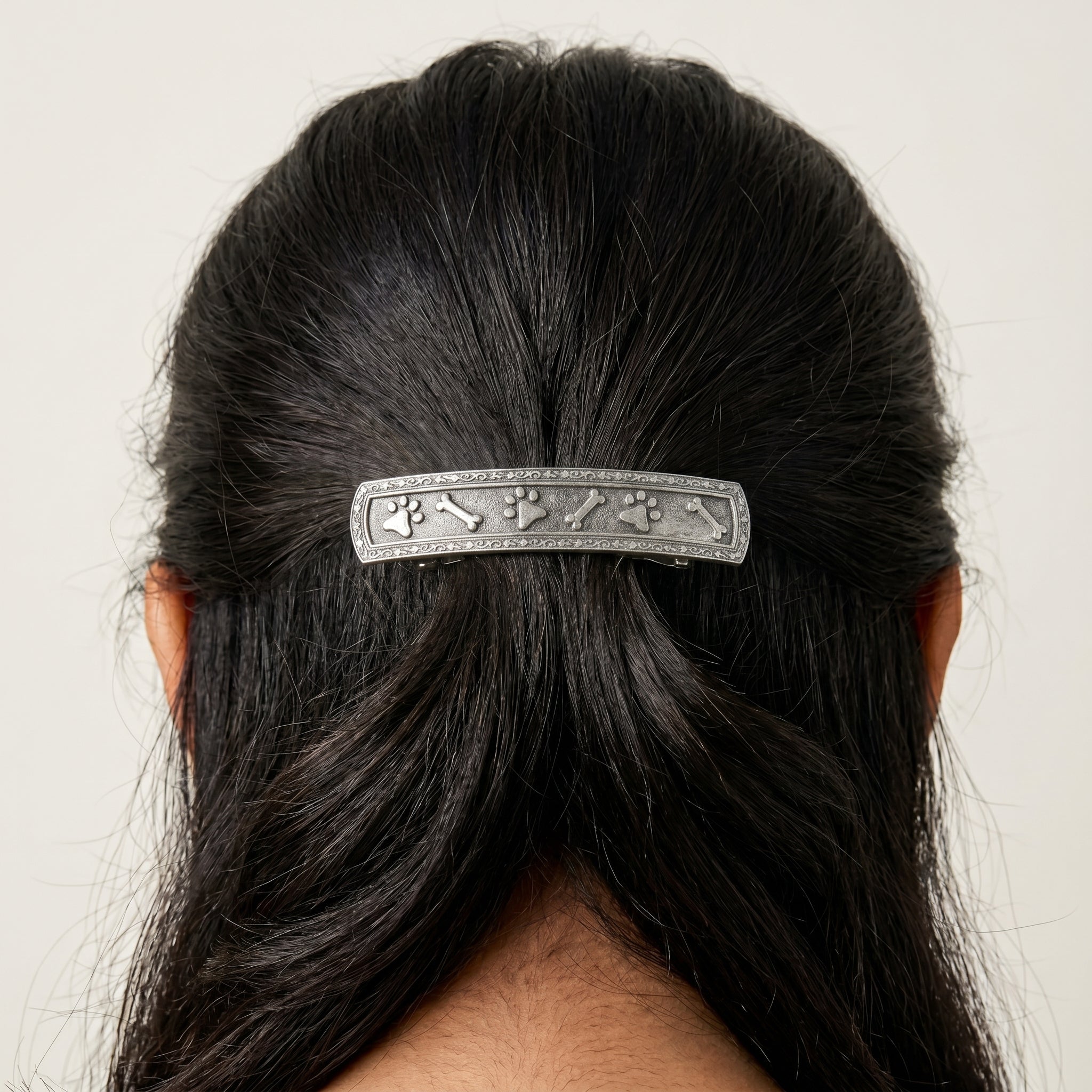 Person with a decorative pet paws and bones themed hair barrette in their black hair on a plain background