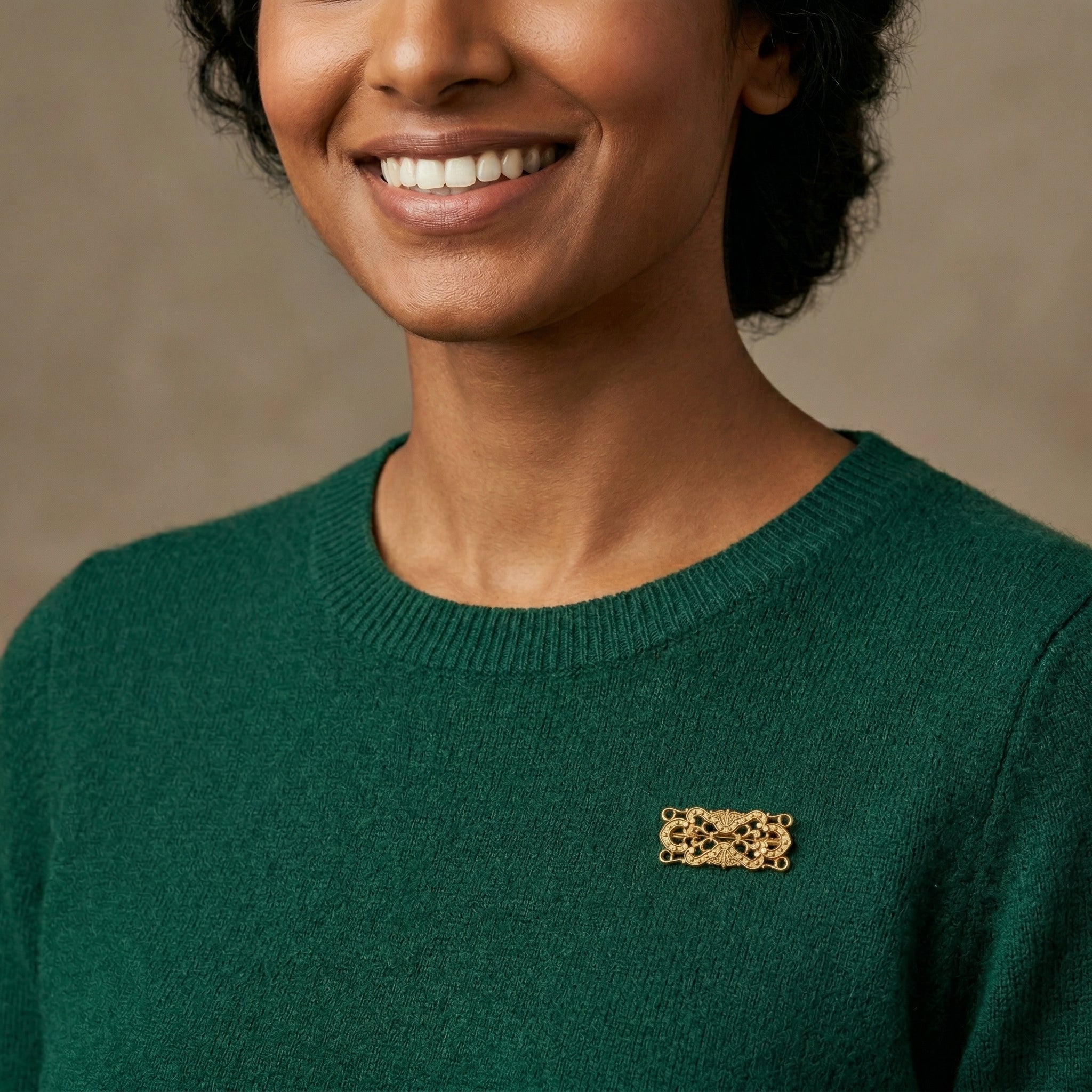 Woman wearing a green sweater with a gold brooch on a beige background