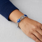 Silver bracelet with blue stones on a wrist against a light gray background