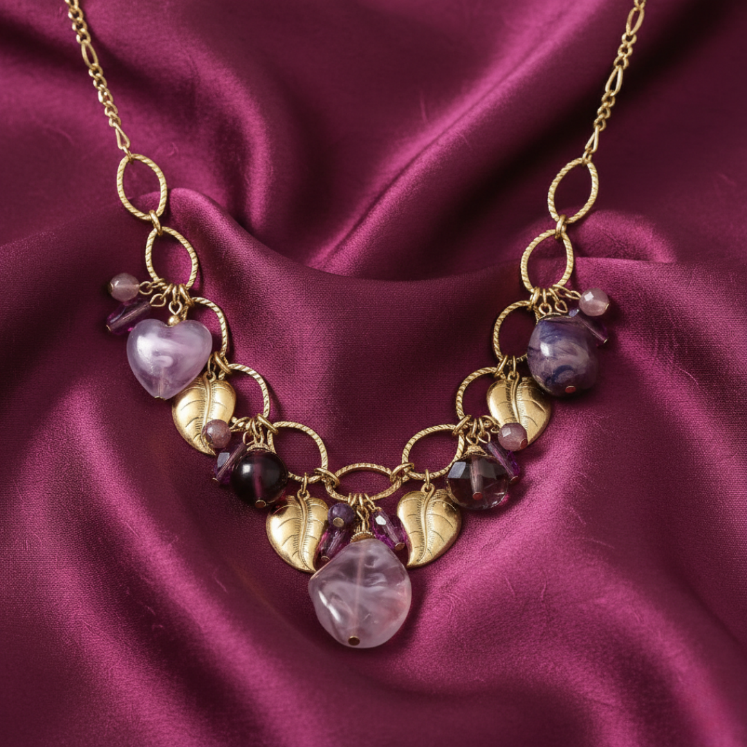 Gold necklace with purple beads on a maroon fabric background