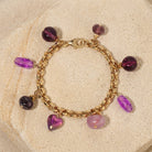 Gold bracelet with various purple beads and charms on a stone surface