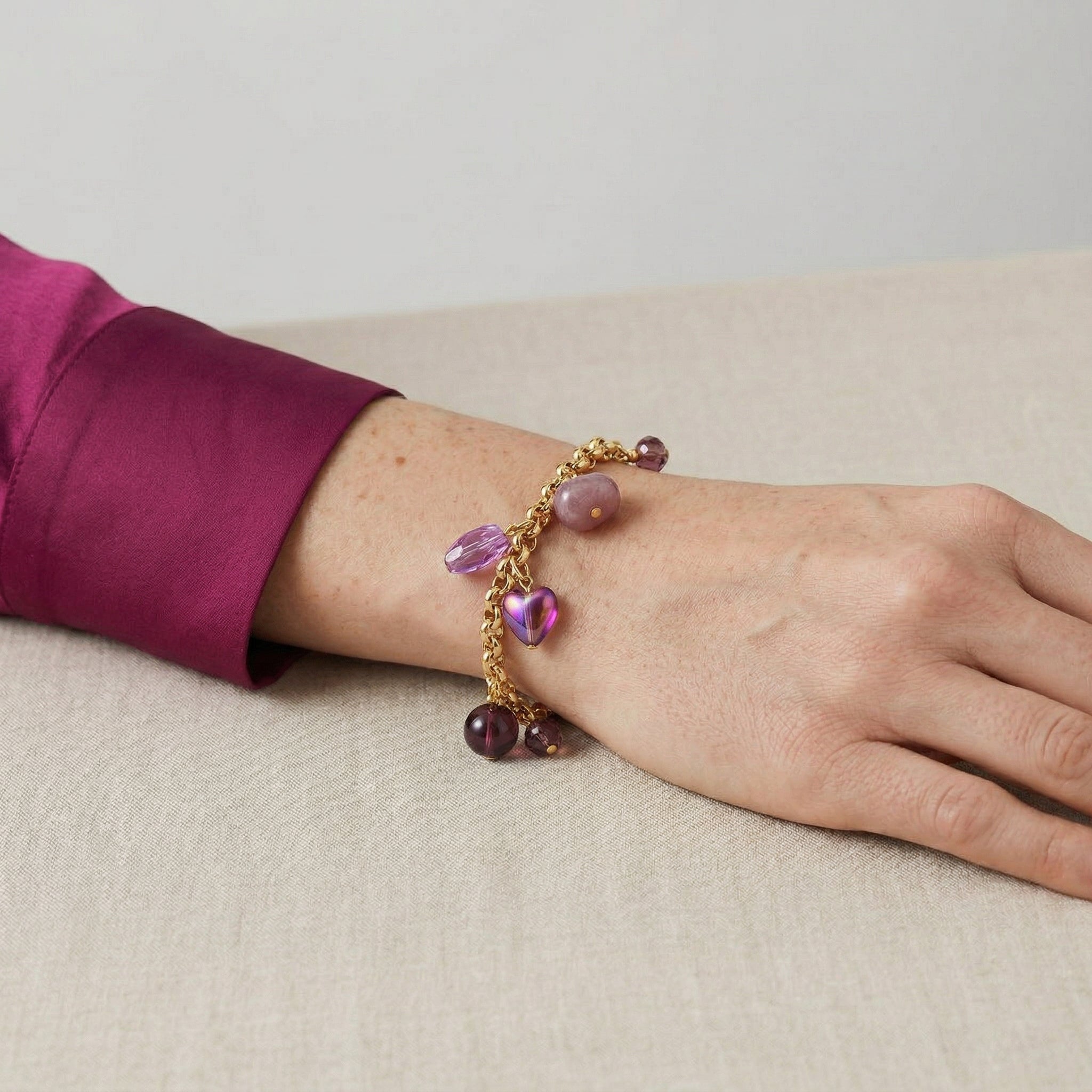 Bracelet with various purple beads and charms on a wrist against a neutral background