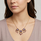 Woman wearing a gold necklace with purple stones and beads on a neutral background