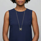 Woman wearing a long necklace with a butterfly locket pendant on a plain background