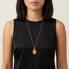 Woman wearing a black sleeveless top with a gold locket necklace featuring a pendant.