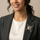 Woman wearing a gray blazer with a decorative brooch on a neutral background