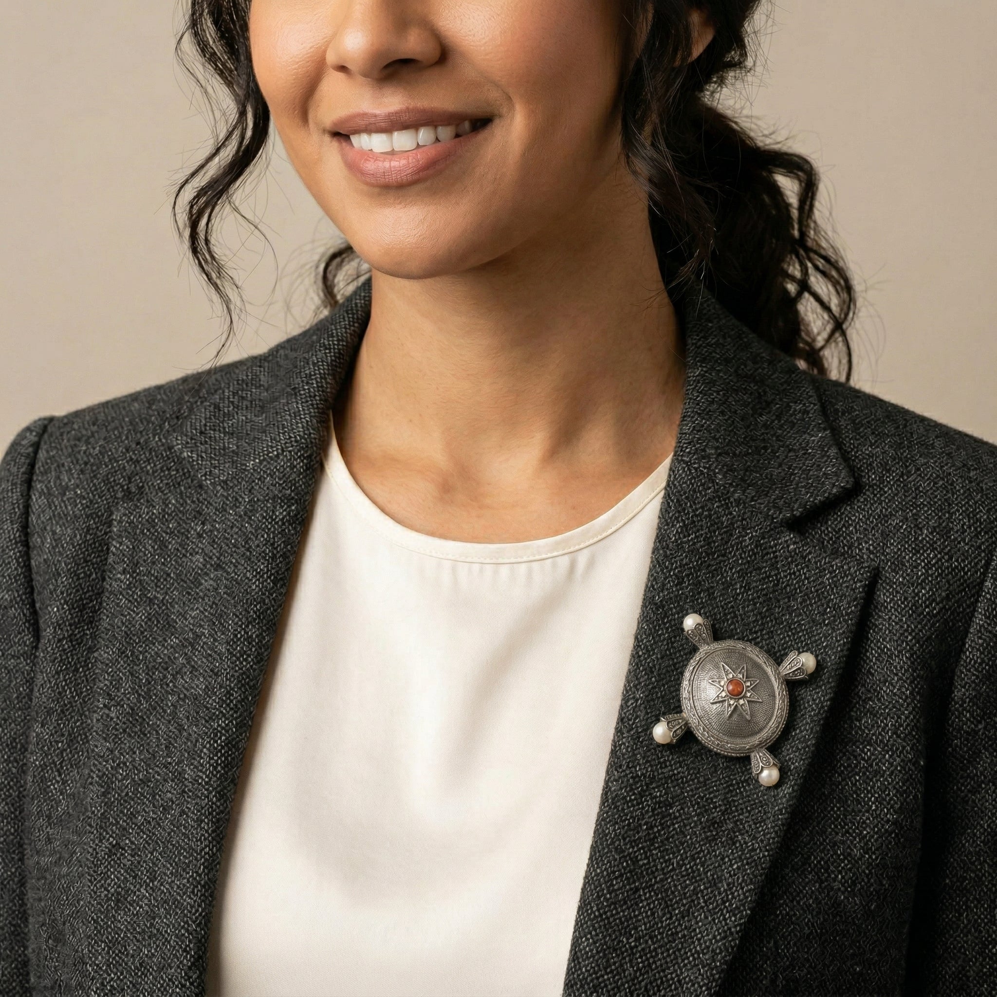 Woman wearing a gray blazer with a decorative brooch on a neutral background