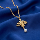 Gold necklace with a bee pendant and pearl on a blue fabric background