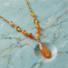 Necklace with orange teardrop pendant on gold chain against a marble background