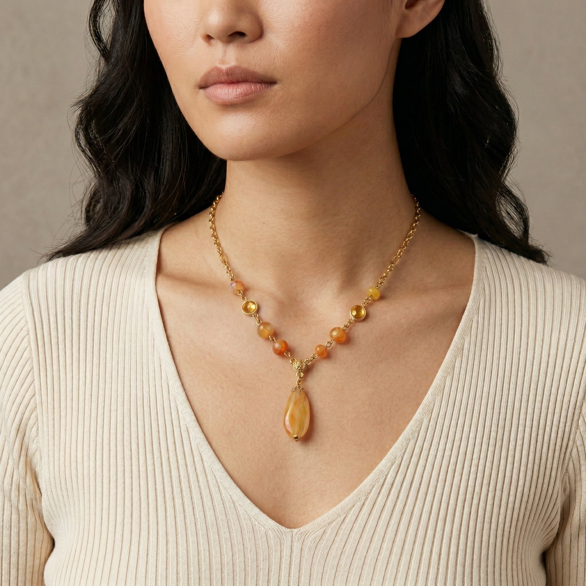 Woman wearing a necklace with amber-colored stones against a neutral background