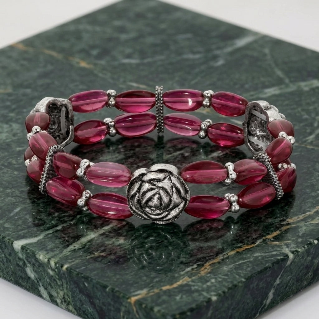 Stack of red beaded bracelets with silver rose accents on a green marble surface