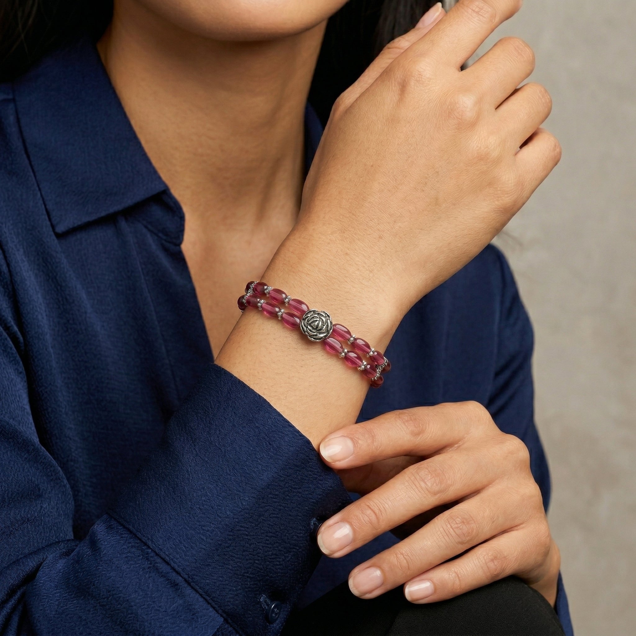 Person wearing a red beaded bracelet with a metal rose design on a neutral background