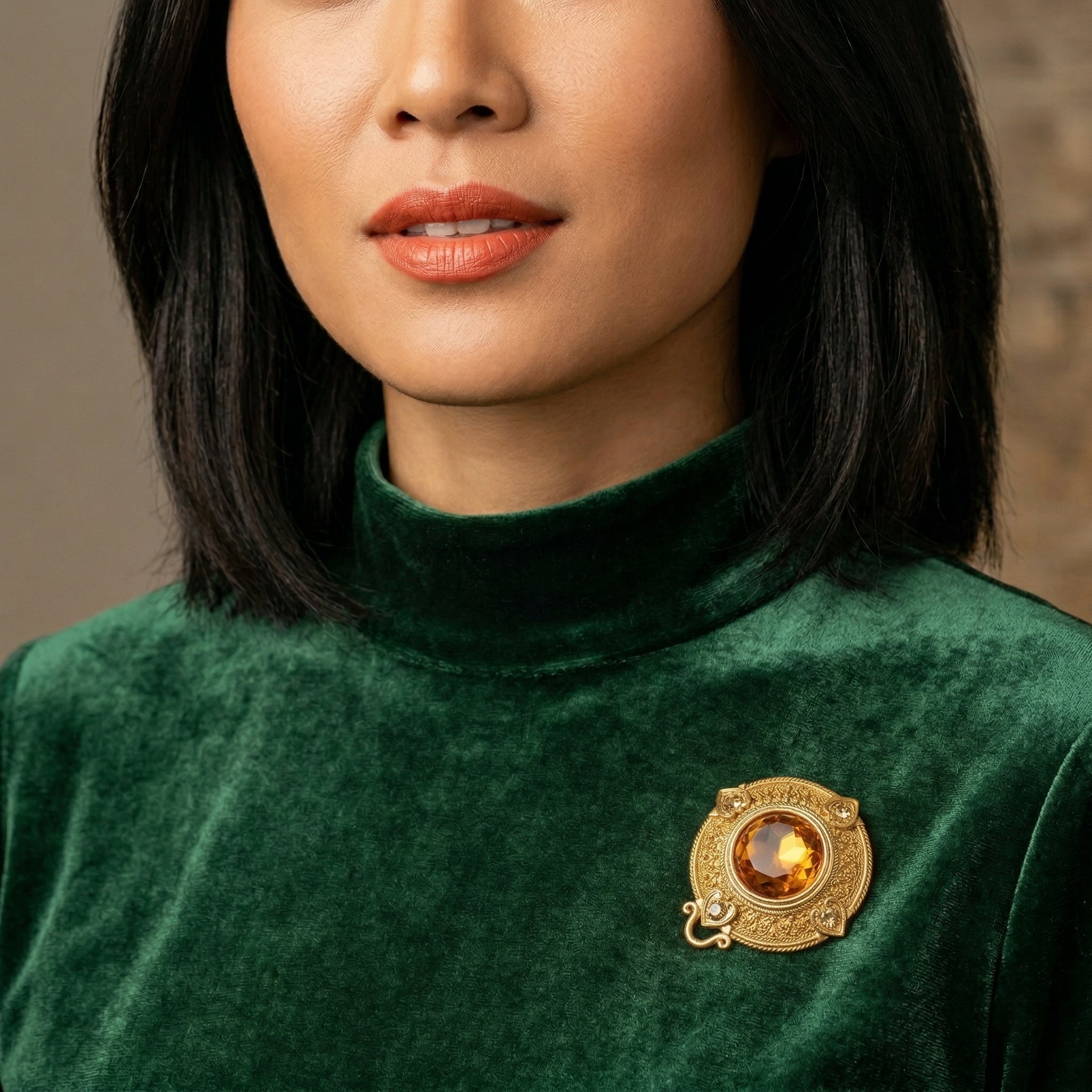 Woman in a green sweater wearing a gold tone brooch pin with giant topaz crystal center and smaller topaz crystal accents