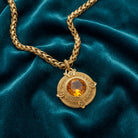 Gold necklace with a topaz pendant featuring a amber stone on a teal fabric background