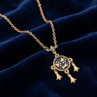 Gold necklace with dog paws and bone design that has a blue pendant on a dark blue velvet background