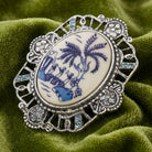 Decorative brooch with blue and white design and light blue sapphire crystals on a green fabric background