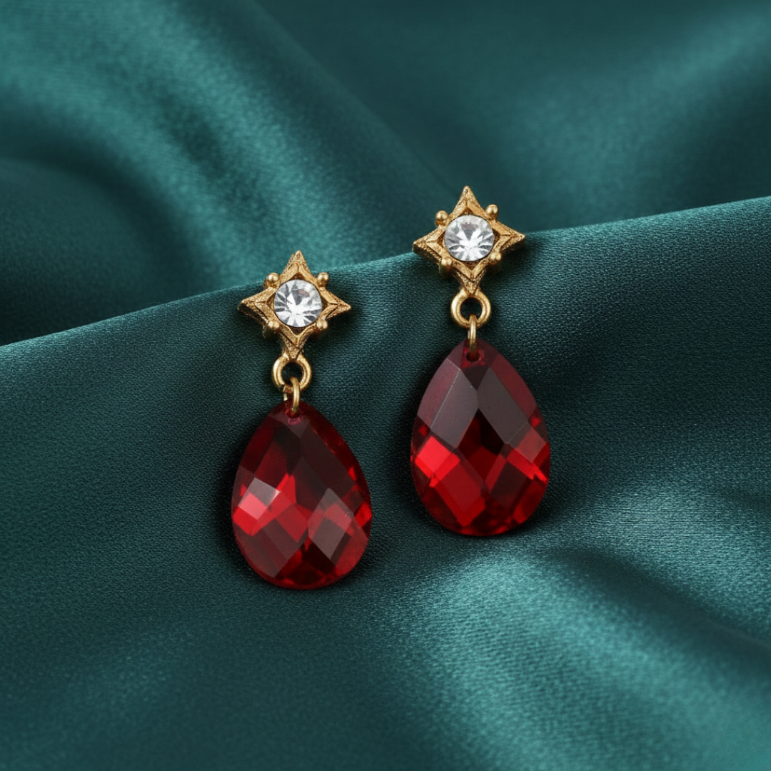 Gold earrings with red teardrop-shaped crystals on a teal fabric background
