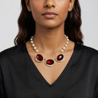 Woman wearing a pearl necklace with large siam red crystals on a plain background