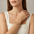 Woman wearing a gold bracelet pink rose stone designs on a neutral background