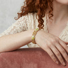 Close-up of a person wearing a gold bracelet with a green floral stone on a neutral background